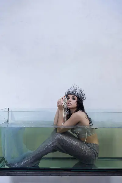 A mermaid sits in a tank of water, wearing a crown and holding a string of pearls. — Stock Photo