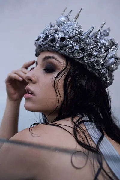 A young woman with dark hair wears a crown of seashells while immersed in water, her face gazing dreamily off to the side. — Stock Photo