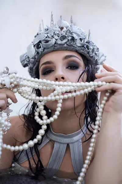 A young woman with dark hair, wearing a crown of seashells and a pearl necklace, poses in a shallow body of water. — Stock Photo