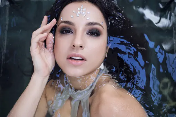 A young woman with dark hair and a shimmering jewel on her forehead floats in an aquarium. — Stock Photo