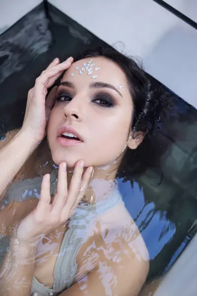 A young woman with dark hair and a jeweled forehead lies submerged in water, creating a captivating underwater scene. — Stock Photo