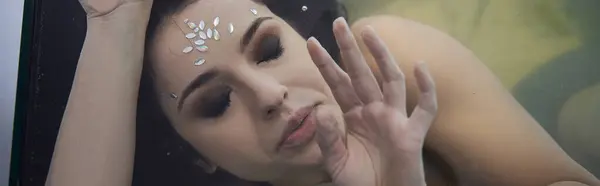 A young woman with dark hair and a jeweled forehead lies submerged in water, her hand outstretched towards the viewer. — Stock Photo