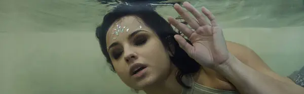 Uma jovem mulher de cabelo escuro, adornada com uma jóia cintilante, flutua sob a superfície da água. — Fotografia de Stock