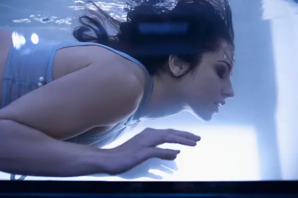 Eine junge Frau mit langen dunklen Haaren schwebt anmutig unter Wasser, die Augen geschlossen und der Ausdruck gelassen. — Stockfoto