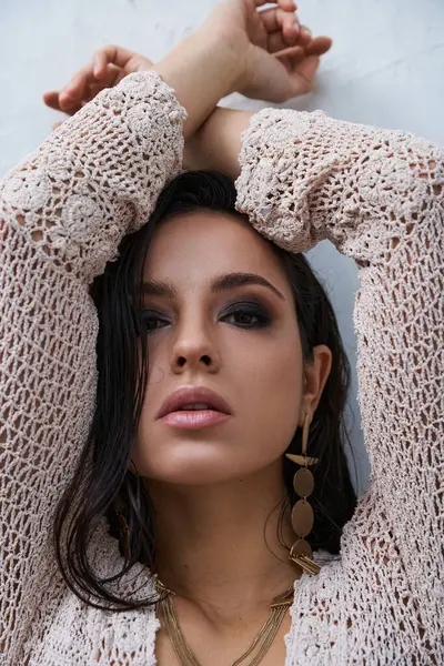 Young woman with dark hair in white knit top poses with arms crossed above head, gazing at the camera. — Stock Photo