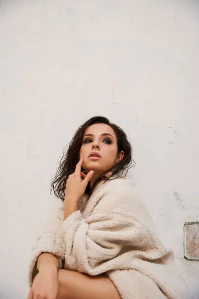 Una joven con el pelo largo y oscuro lleva un abrigo de peluche blanco y posa en un estudio. - foto de stock