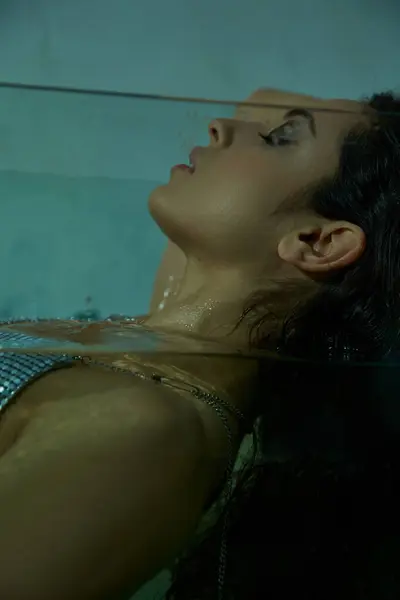 A woman with dark hair lays submerged in a clear studio setting, with water dripping down her face. — Stock Photo