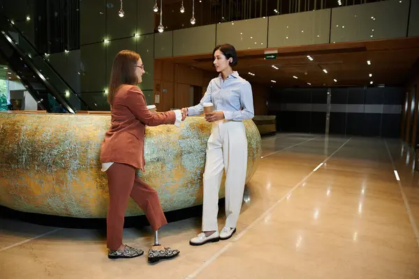Two colleagues, one with a prosthetic leg, stand in an office lobby and chat. — Stock Photo