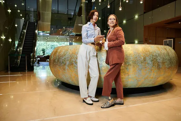 Due colleghi chiacchierano davanti a un grande bancone decorativo nella hall di un ufficio. — Foto stock