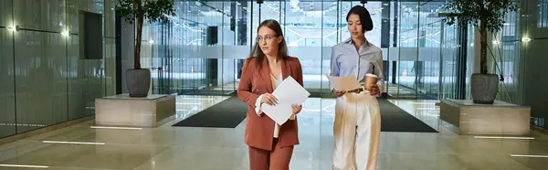 Two colleagues chat and walk through a modern office lobby. — Stock Photo