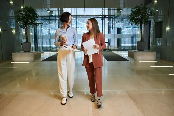 Two colleagues, one with a prosthetic leg, walk and chat in a modern office lobby. — Stock Photo