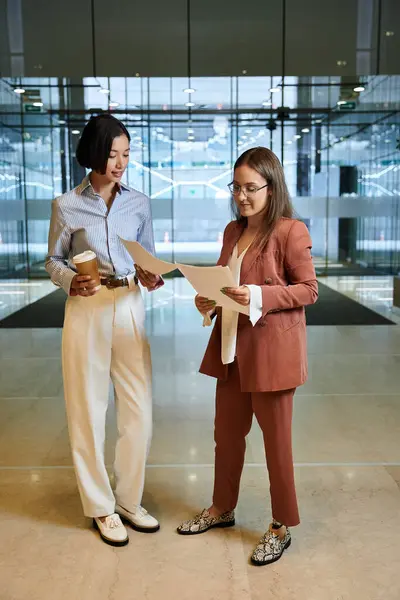 Dos colegas, uno con una pierna protésica, revisan documentos en un vestíbulo de la oficina, mostrando diversidad e inclusión en el lugar de trabajo. - foto de stock