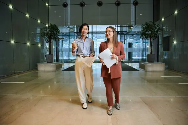 Two women, one with a prosthetic leg, chat and walk together in a modern office lobby. — Stock Photo