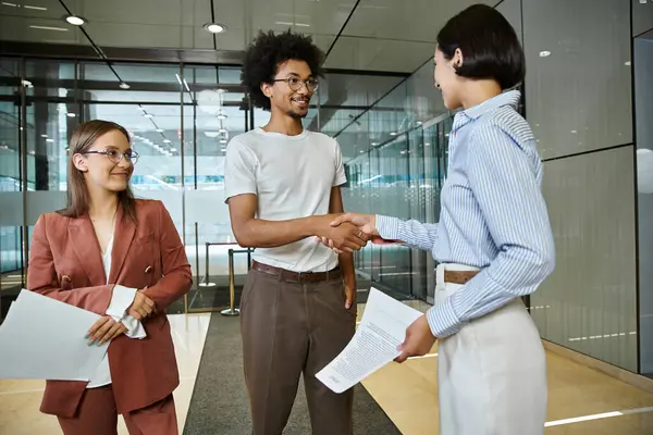 Three colleagues chat and shake hands in an office lobby. — Stock Photo