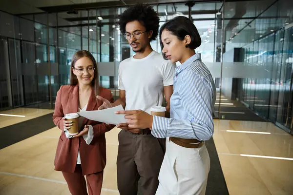 Three colleagues, including a woman with a prosthetic leg, stand in an office lobby and discuss paperwork. — Stock Photo