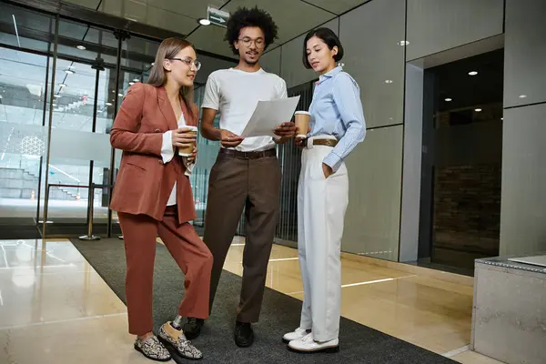 Three colleagues chat and review paperwork in an office lobby, one woman with a prosthetic leg. — Stock Photo