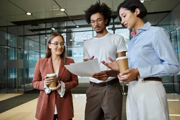 Three colleagues, stand in a modern office lobby, engaged in a conversation. — Stock Photo