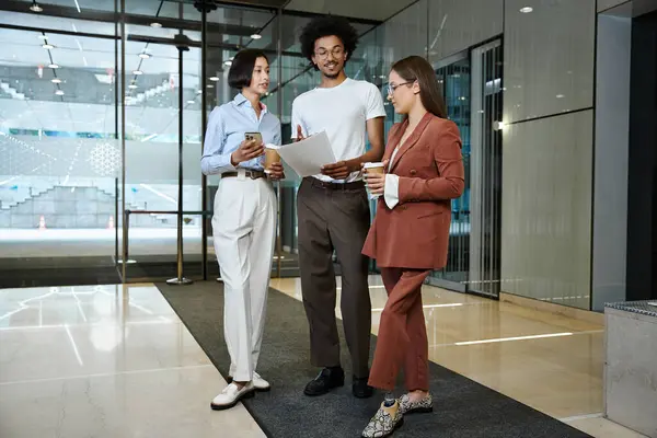 Three colleagues, including a woman with a prosthetic leg, stand in an office lobby and engage in a friendly conversation. — Stock Photo