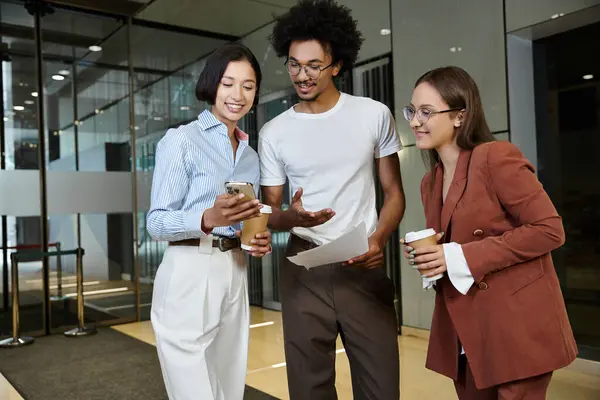 Three colleagues, engage in a friendly conversation in a modern office lobby. — Stock Photo