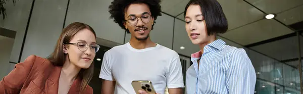 Three colleagues, gather in the office lobby and discuss something on a smartphone. — Stock Photo
