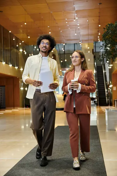 Zwei Kollegen, ein Mann und eine Frau, gehen und plaudern in einer Büro-Lobby. — Stockfoto