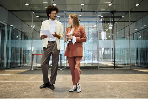 Two colleagues, a man and a woman, chat in the lobby of an office building. — Stock Photo