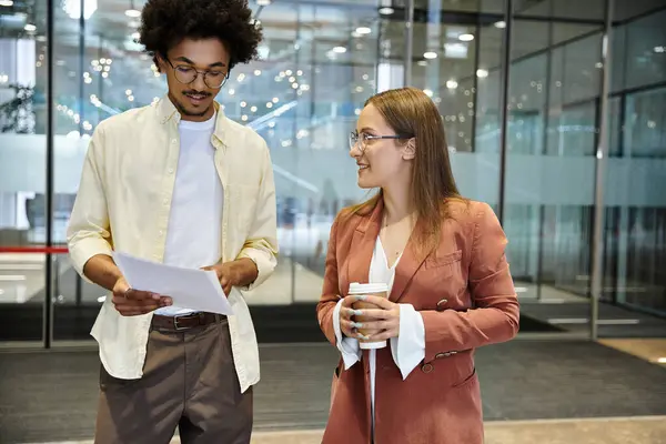 A man and woman, chat casually while holding a document and coffee, creating a friendly and diverse atmosphere. — Stock Photo