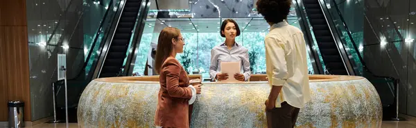 Tre colleghi chiacchierano in una hall dell'ufficio, con una scala mobile sullo sfondo, mostrando la diversità. — Foto stock