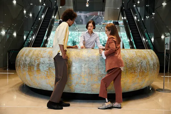 Three colleagues, including a woman with a prosthetic leg, chat and laugh together at a reception desk in an office building lobby. — Stock Photo