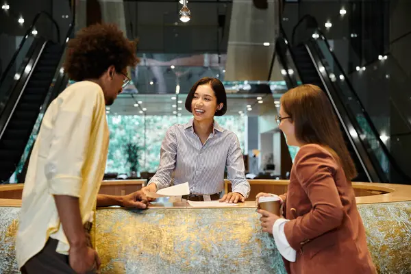 Three colleagues, stand near a reception desk, smiling and talking. — Stock Photo