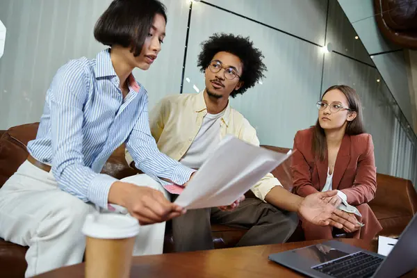 Three colleagues sit on a couch in an office lobby and discuss a document. — Stock Photo