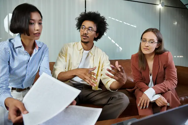 Three colleagues discuss documents while sitting on a couch in an office lobby. — Stock Photo