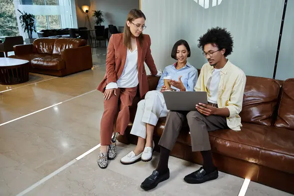 Um grupo de colegas multiculturais relaxar em um sofá de couro em um lobby de escritório moderno, compartilhando uma risada e uma pausa para café. — Fotografia de Stock