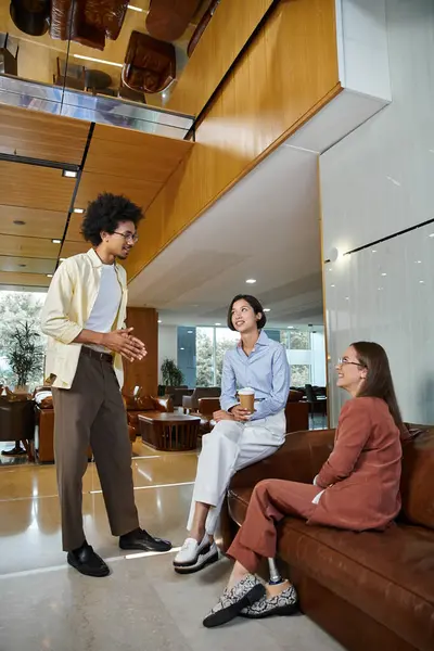 Three colleagues chat and laugh together in an office lobby. — Stock Photo