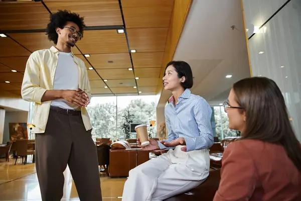 Three colleagues chat in the office lobby. One woman is holding a coffee cup — Stock Photo