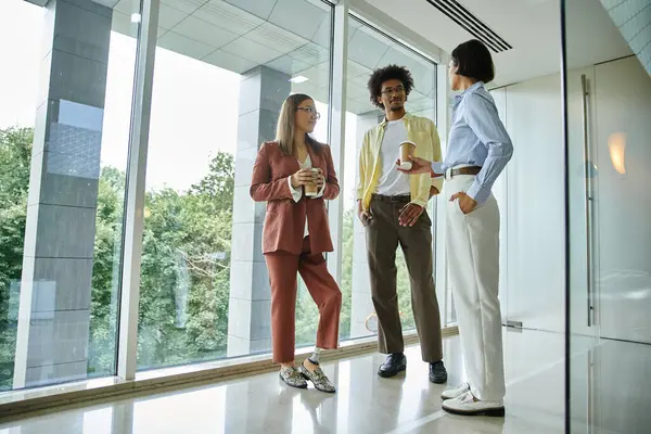 Three colleagues, including a woman with a prosthetic leg, stand near a window in a modern office, smiling and talking. — Stock Photo