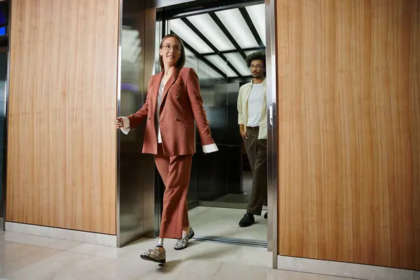 Uma mulher com uma perna protética sai de um elevador e sorri calorosamente perto do colega que está saindo. — Fotografia de Stock