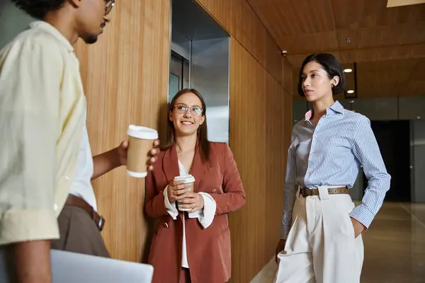 Three colleagues stand by an elevator, smiling and chatting. — Stock Photo