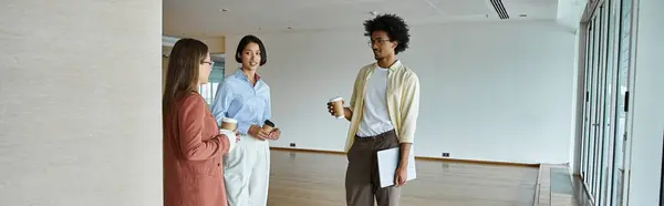 Three colleagues converse and enjoy coffee in a modern office setting. — Stock Photo