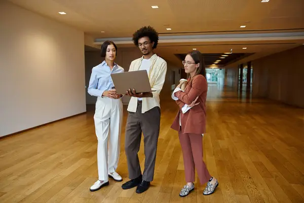 Three diverse colleagues converse in a modern office, showcasing inclusivity and teamwork. — Stock Photo