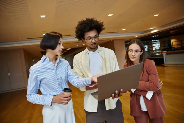 Three colleagues stand together in a modern office, discussing work while looking at a laptop. — Stock Photo