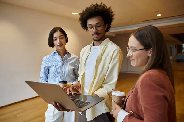 Trois collègues discutent du travail sur un ordinateur portable dans un environnement de bureau contemporain. — Photo de stock