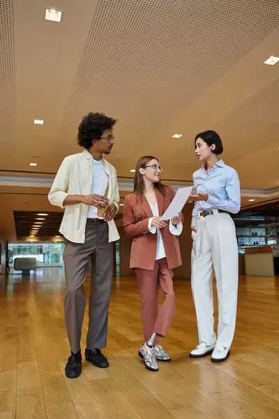 Three colleagues stand together in a modern office setting, engaging in a lively discussion. — Stock Photo