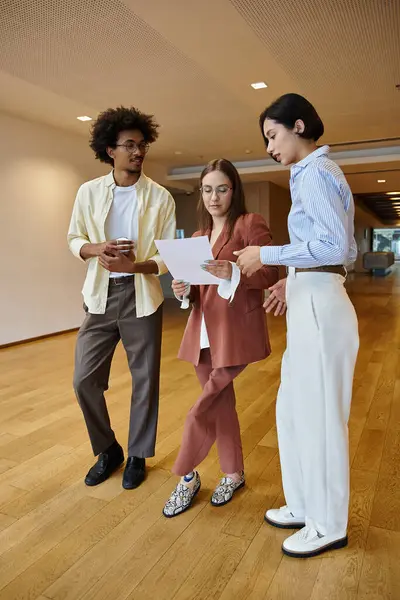 Three diverse colleagues chat and review documents in a modern office setting. — Stock Photo