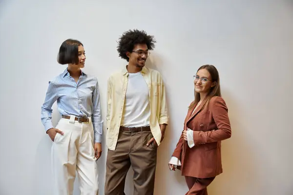 Tres colegas están en una oficina moderna, sonriendo y charlando entre sí. - foto de stock