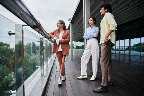 Three colleagues, including one with a prosthetic leg, chat and laugh on a modern office rooftop terrace. — Stock Photo