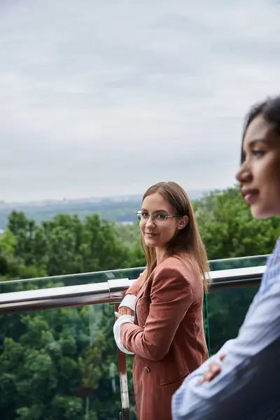 Two diverse colleagues stand on a rooftop terrace, chatting and enjoying the view. — Stock Photo