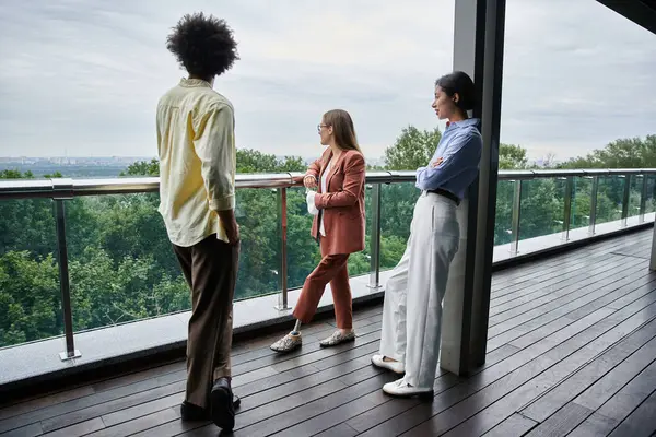 Three colleagues, including a woman with a prosthetic leg, chat on a modern office rooftop terrace with a view of the city. — Stock Photo