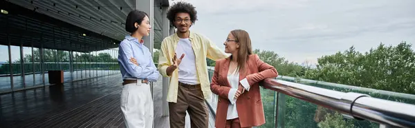 Three colleagues stand on a rooftop terrace, chatting and laughing. — Stock Photo