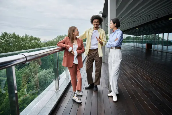 Three colleagues, including a woman with a prosthetic leg, chat and laugh while standing on a rooftop terrace. — Stock Photo